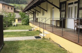 Außenansicht eines gelben Gebäudes mit Veranda und Berg im Hintergrund.