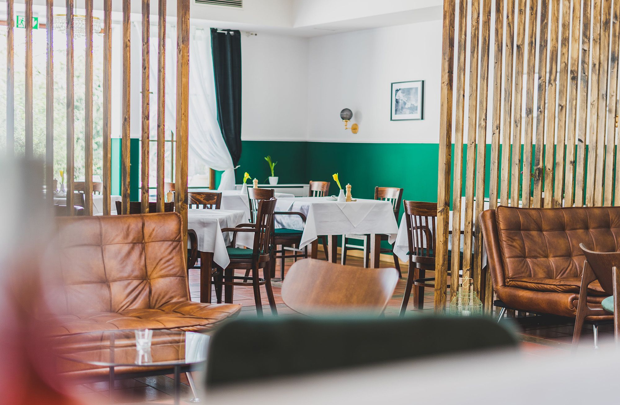 Ein stilvoll eingerichteter Gastraum mit Holzmöbeln, grünen Wänden und weißen Tischdecken.