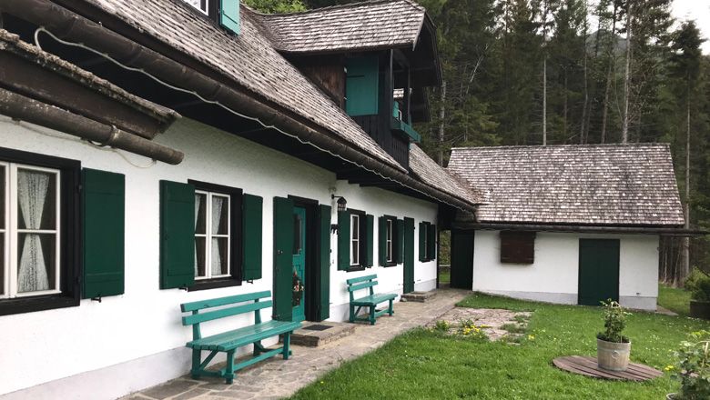 Ein traditionelles Ferienhaus mit grünen Fensterläden und Holzbänken vor einem Wald.