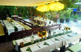 Gedeckte Tische im Freien mit Sonnenblumen und gelben Sonnenschirmen.