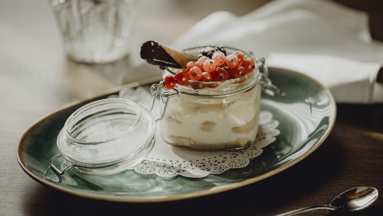 Dessert im Glas mit roten Johannisbeeren und Schokoladenkeks auf gr&uuml;nem Teller.