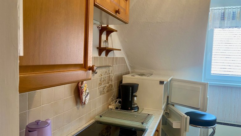 Kleine Küche mit Holzschränken, Herd, Kaffeemaschine und offenem Kühlschrank.