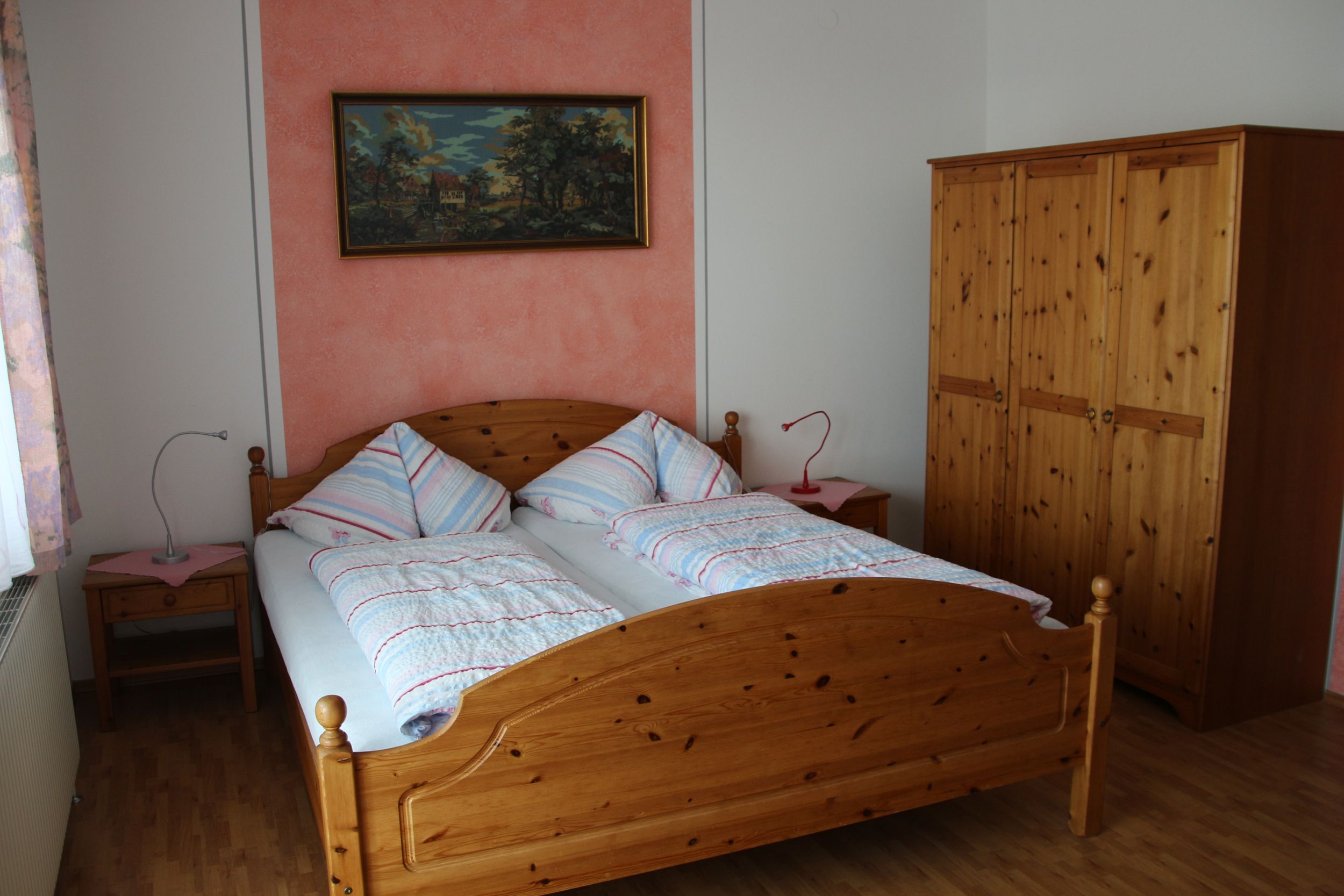 Ein Schlafzimmer mit einem Doppelbett, zwei Nachttischen, einem Kleiderschrank und einem Gemälde an der Wand.