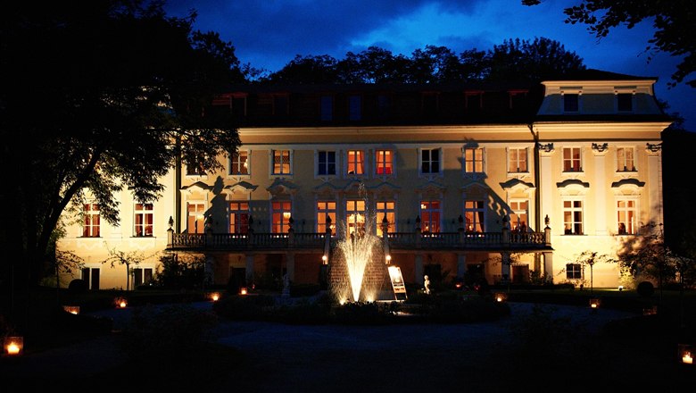 Beleuchtetes Schloss Stuppach bei Nacht mit Springbrunnen im Vordergrund.