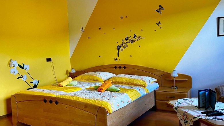 Gemütliches Schlafzimmer mit gelber Wand, Doppelbett und dekorativen Schmetterlingen an der Wand.