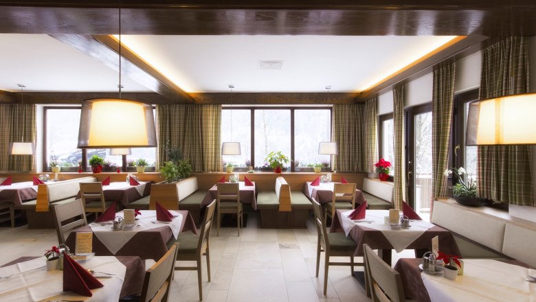 Innenansicht eines gemütlichen Restaurants mit Holzmöbeln, gedeckten Tischen und großen Fenstern.