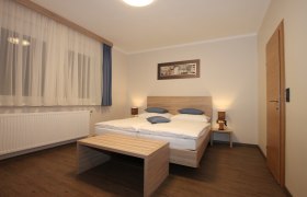 Ein schlicht eingerichtetes Zimmer mit Doppelbett, Holzm&ouml;beln und Vorh&auml;ngen.