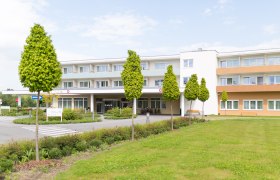 Außenansicht eines modernen Gebäudes mit Bäumen und Rasenfläche.