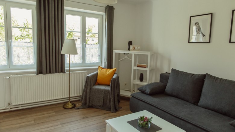 Helles Wohnzimmer mit grauem Sofa, Sessel, Stehlampe und weißen Möbeln.