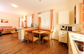 Helles Zimmer mit Holzboden, Esstisch, K&uuml;che und Bett.