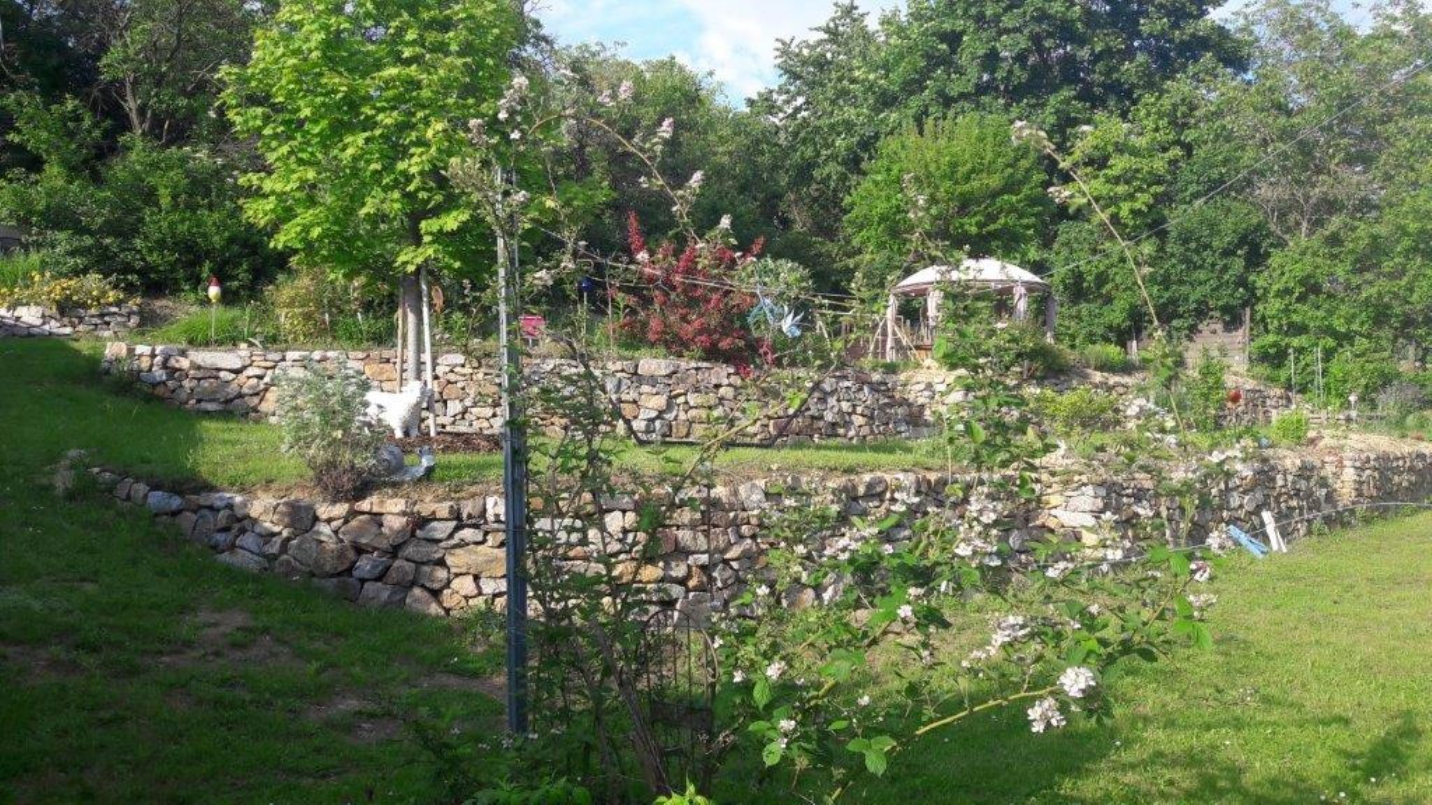 Terrassierter Garten mit Steinmauern und Pavillon.