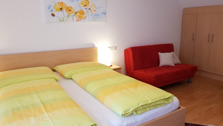 Ein Doppelzimmer mit einem Bett, einem roten Sofa, einem Schrank und einem Bild an der Wand.