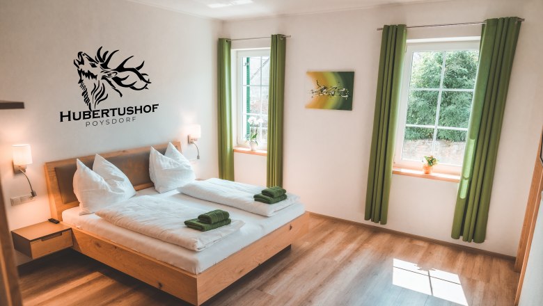 Modernes G&auml;stezimmer mit Doppelbett, gr&uuml;nen Vorh&auml;ngen und Wanddekoration im Hubertushof Poysdorf.