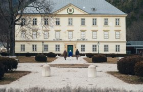 Umgeben von einer malerischen Winterlandschaft, strahlt das Schloss Reichenau eine zeitlose Eleganz aus. Die schneebedeckten Str&auml;ucher und der klare Himmel schaffen eine friedliche Atmosph&auml;re, die zum Verweilen einl&auml;dt. Ein perfekter Ort, um die winterliche Sch&ouml;nheit der Wiener Alpen zu genie&szlig;en.