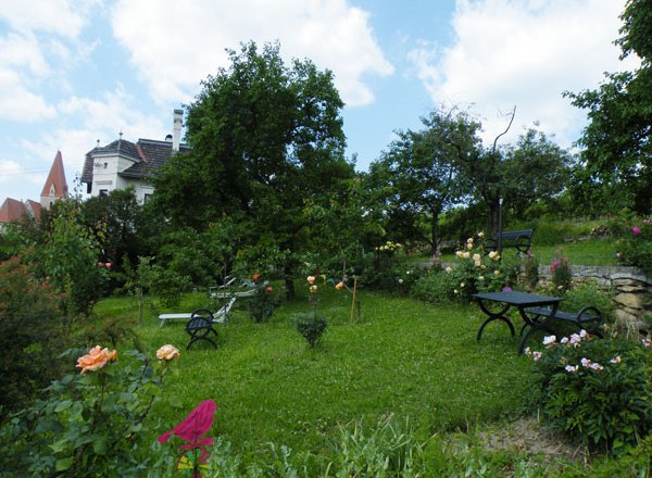 Garten, © Fam. Probst Ein grüner Garten mit Bäumen, Blumen und Sitzbänken unter blauem Himmel.