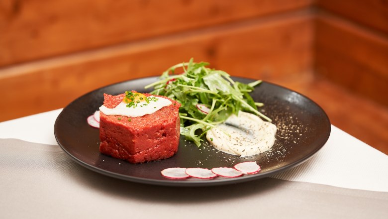 Ein Teller mit Beef Tartar, Salat und Sauce, dekoriert mit Radieschenscheiben.