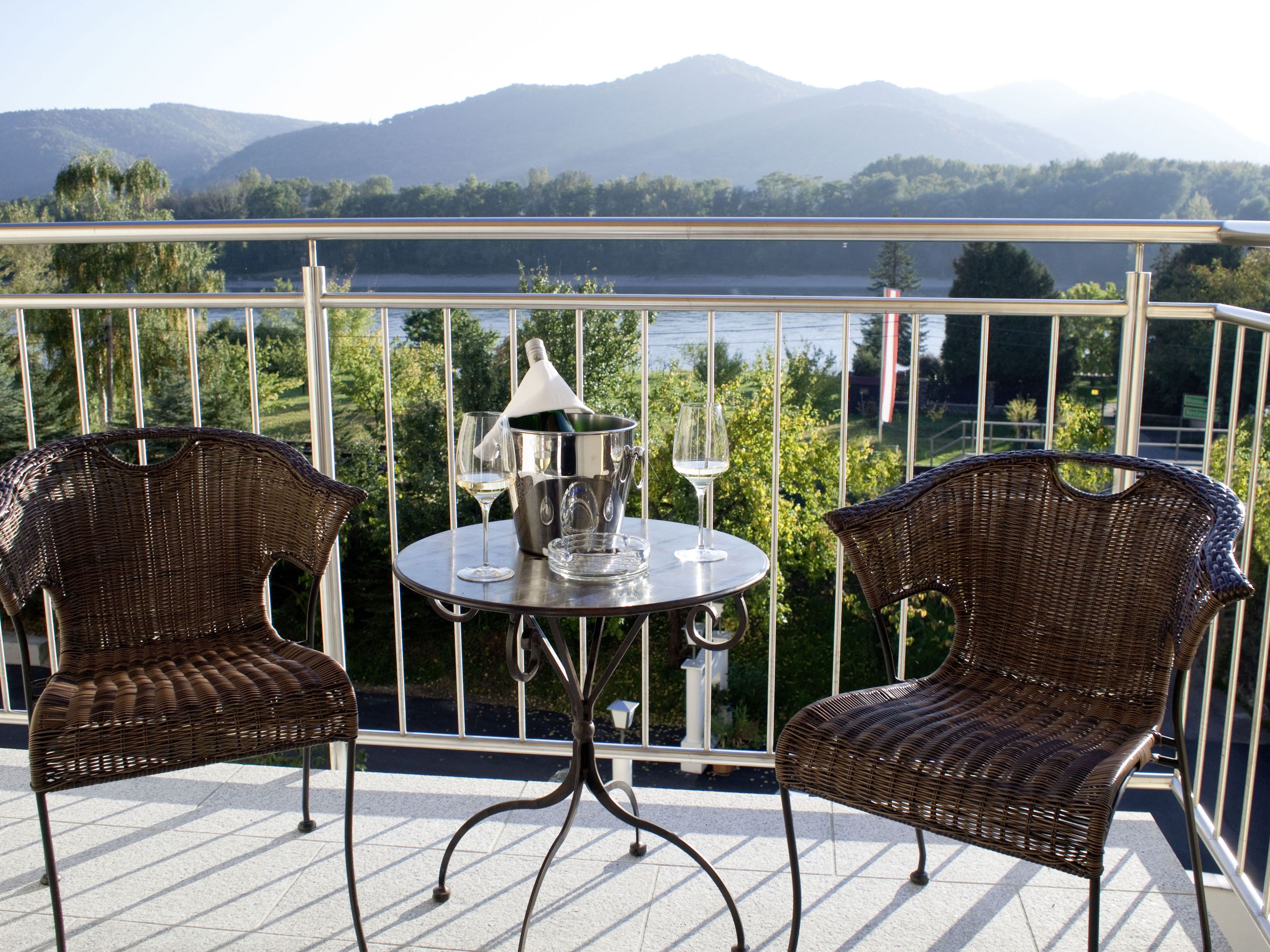 Zwei Rattanstühle und ein Tisch mit Sektkühler auf einer Terrasse mit Bergblick.