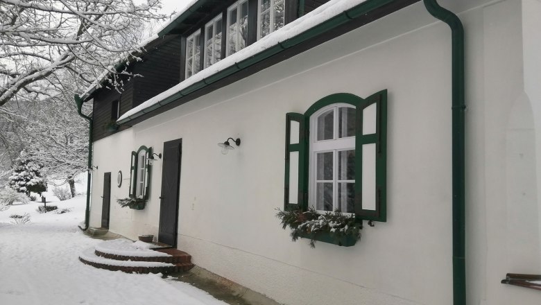 Ein verschneites Haus mit gr&uuml;nen Fensterl&auml;den und Dachrinnen.