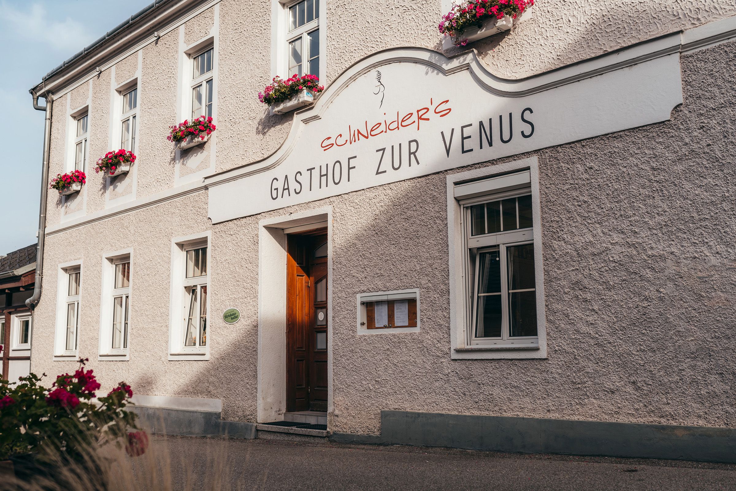 Gasthof zur Venus mit blumengeschmückter Fassade und Holztür.