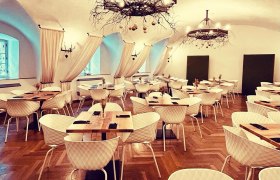 Eleganter Speisesaal mit Parkettboden, wei&szlig;en St&uuml;hlen, Holztischen und dekorativen Kronleuchtern.