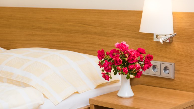 Gästezimmer, © Familie Graf Ein Gästezimmer mit einem Bett, einer Nachttischlampe und einem Blumenstrauß in einer Vase auf dem Nachttisch.