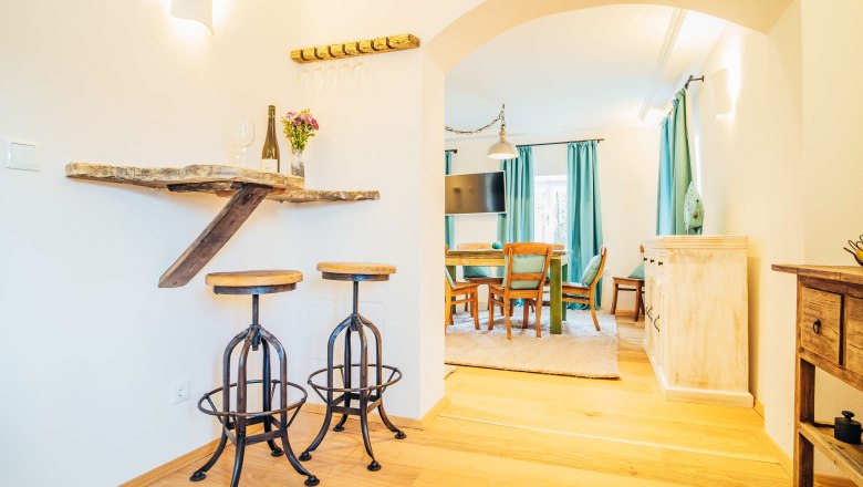 Gem&uuml;tliches Wohnzimmer mit Holzm&ouml;beln, Barhockern und Esstisch.