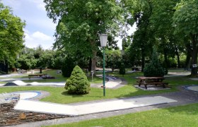 Minigolfplatz mit B&auml;umen und B&auml;nken in einem Park.
