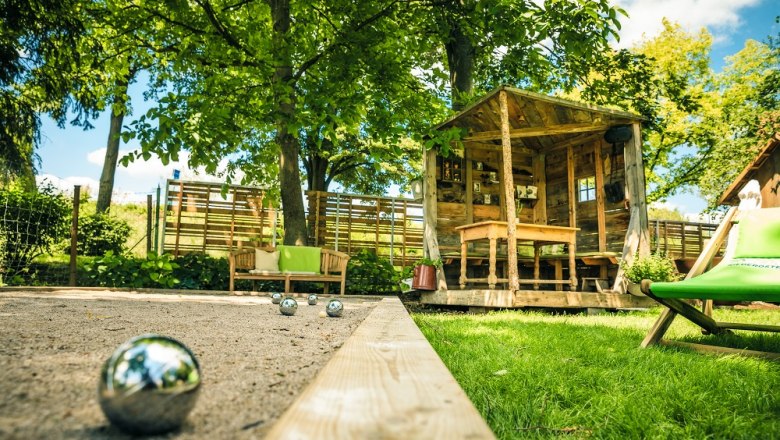 Garten mit Laube und Sandfläche mit Boccia Kugel, daneben Liegestuhl