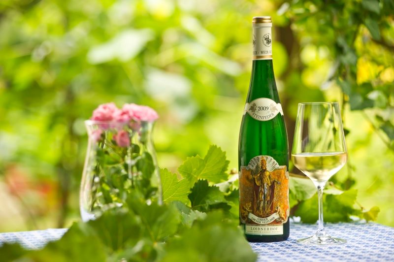 Weinflasche und Glas auf Tisch mit Blumen und Blättern im Hintergrund.