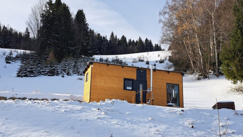 Kleines Holzhaus im Schnee vor einem Wald.