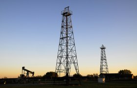 Zwei Bohrt&uuml;rme und eine &Ouml;lpumpe bei Sonnenuntergang.