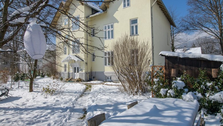 Schneebedeckter Garten mit Tisch und Stühlen vor einem gelben Haus.