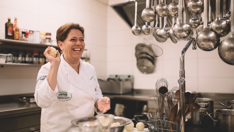 Eine lachende K&ouml;chin in einer professionellen K&uuml;che, die einen Teigball in der Hand h&auml;lt.