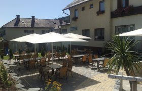 Außenbereich einer Pension mit Tischen, Stühlen und Sonnenschirmen.
