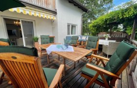 Holzterrasse mit Tisch, gemütlichen Stühlen und Sonnenschutz.