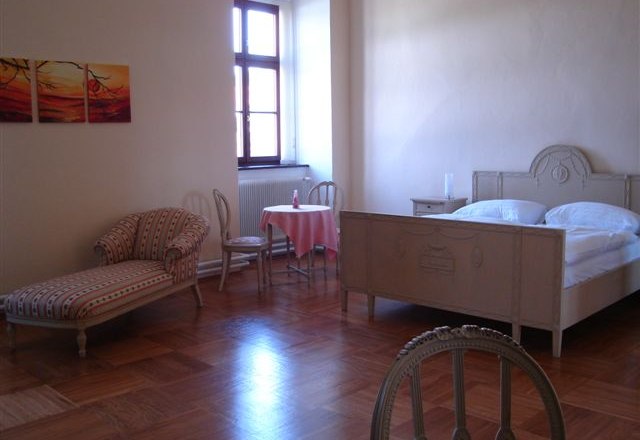 Helles G&auml;stezimmer mit antikem Bett, Chaiselongue und kleinem Tisch.