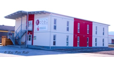 Zweist&ouml;ckiges Motelgeb&auml;ude mit rotem und wei&szlig;em Anstrich, Au&szlig;entreppe und gro&szlig;em Schild mit der Aufschrift 'Motel'.