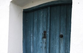 Blaue Holzt&uuml;r in einem wei&szlig;en Geb&auml;ude mit Kopfsteinpflaster davor.