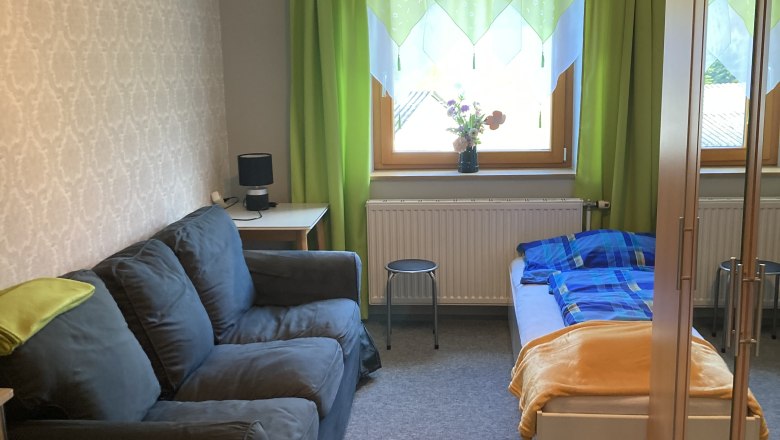 Ein gem&uuml;tliches Schlafzimmer mit Sofa, Bett, Schrank und gr&uuml;nem Vorhang.