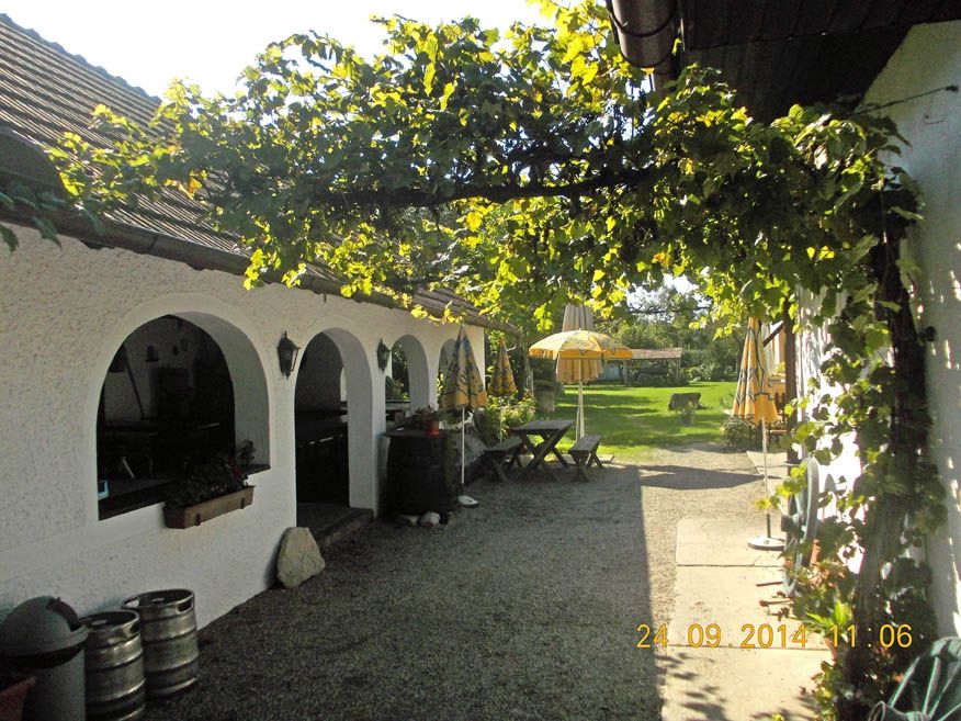 Ein gemütlicher Gasthof mit weißen Bögen, grüner Laube und gelben Sonnenschirmen im Garten.