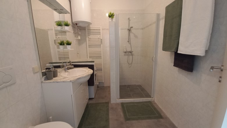 Modernes Badezimmer mit Dusche, Waschbecken, Spiegel und Handtüchern.