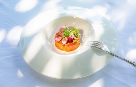 Ein kunstvoll angerichtetes Gericht auf einem wei&szlig;en Teller mit einer Gabel daneben.