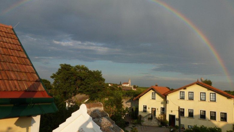 Gästehaus Fam. Springer, © Gästehaus Springer Ein Regenbogen über einem Dorf mit gelben Häusern und roten Dächern.