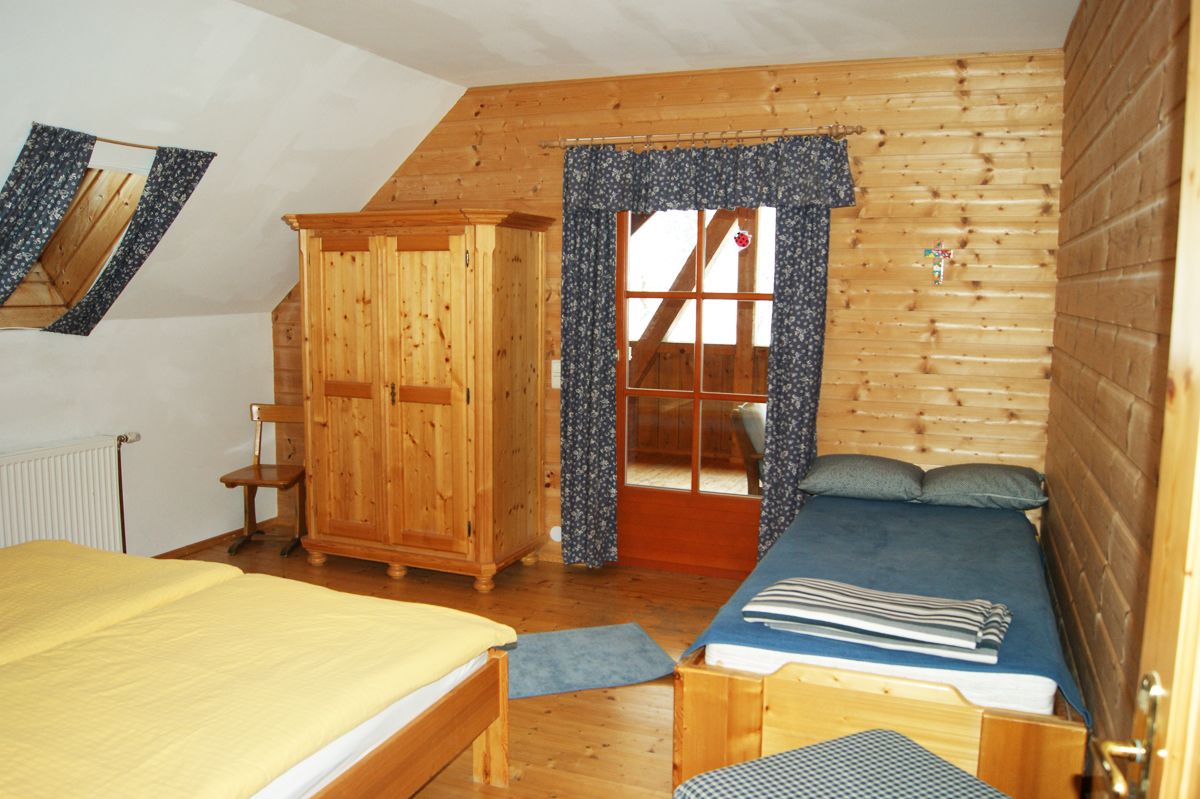 Innenansicht eines rustikalen Schlafzimmers mit Holzwänden, einem Doppelbett, einem Einzelbett und einem Kleiderschrank.