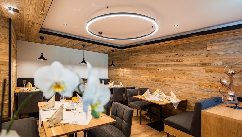 Gemütliches Restaurant mit Holzwänden, modernen Leuchten und elegant gedeckten Tischen.
