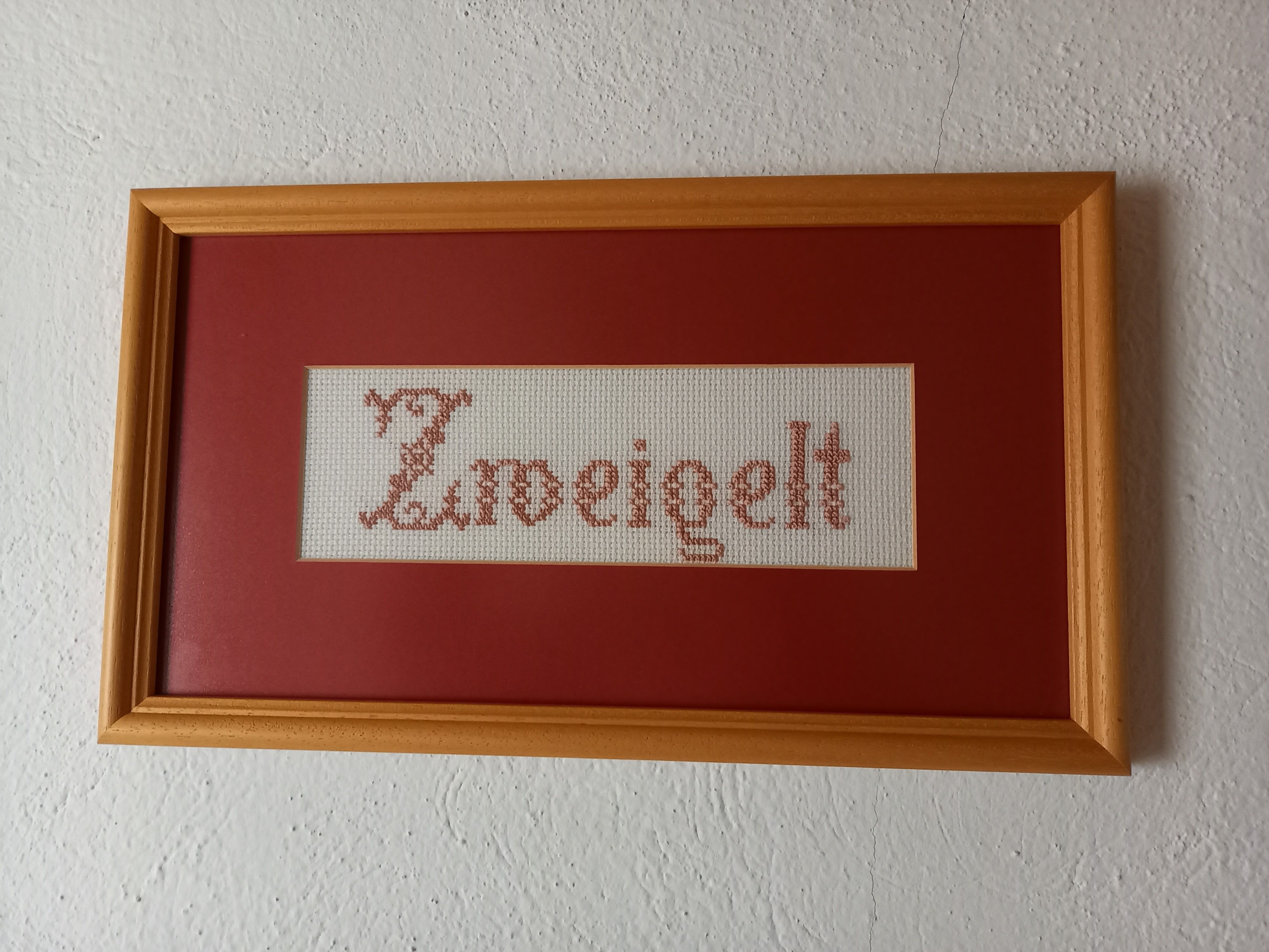 Stickbild mit dem Wort 'Zweigelt' in einem Holzrahmen.