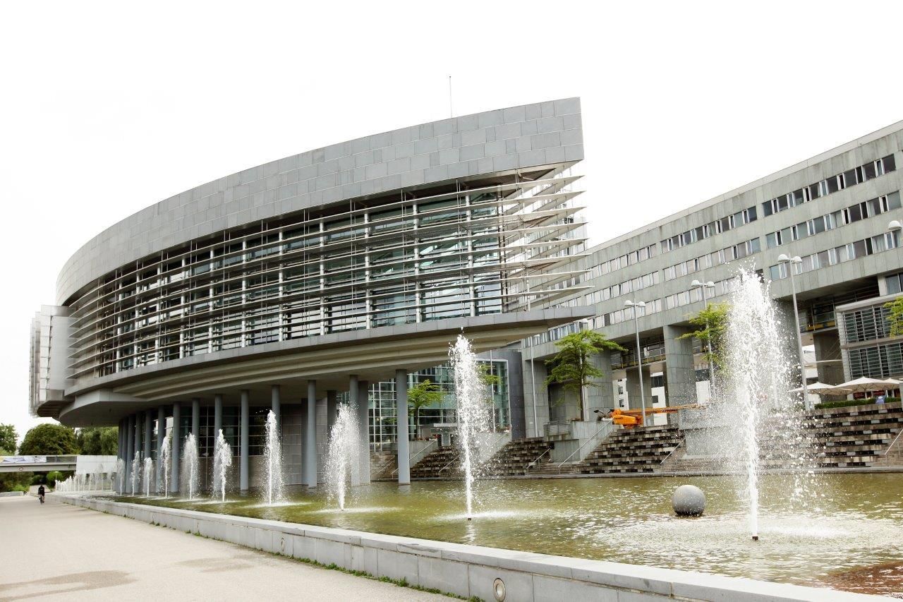 Modernes Gebäude mit Glasfassade und Springbrunnen im Vordergrund.