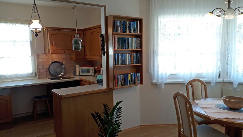 Gem&uuml;tliche K&uuml;che mit Holzm&ouml;beln, Esstisch und B&uuml;cherregal.