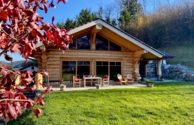 Holzchalet mit Terrasse und roten Herbstblättern im Vordergrund.