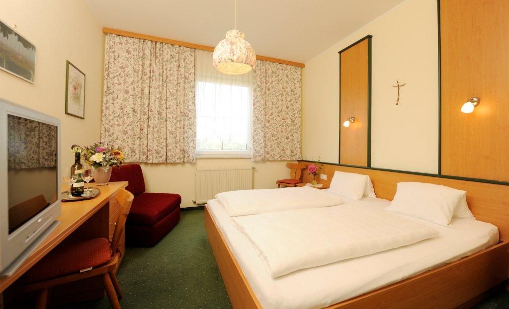 Gemütliches Hotelzimmer mit Doppelbett, TV, Blumen und Vorhängen.